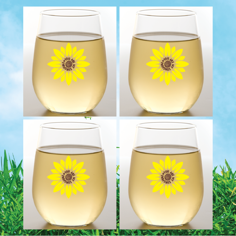 Four wine glasses with sunflower designs on a grass and blue sky background